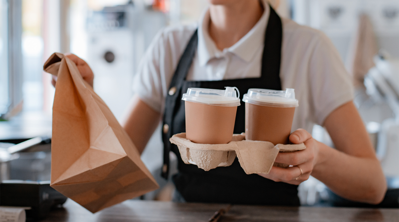 Image of a fast food worker handing over coffees and a bag of food to support fast food minimum wage article