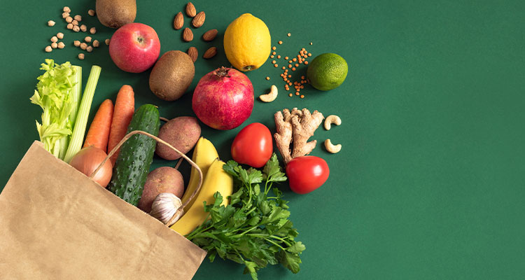 Brown paper bag full of fruit & veg on a green background
